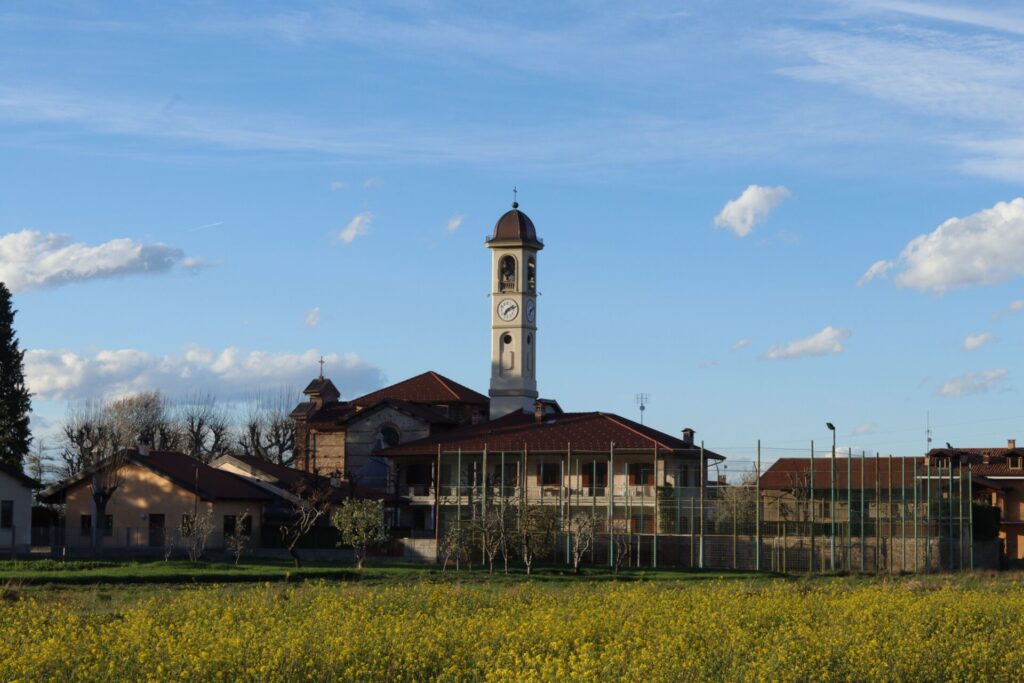 Charming view of the church tower in Mellana, Piemonte, set against a vivid sky and blooming field.