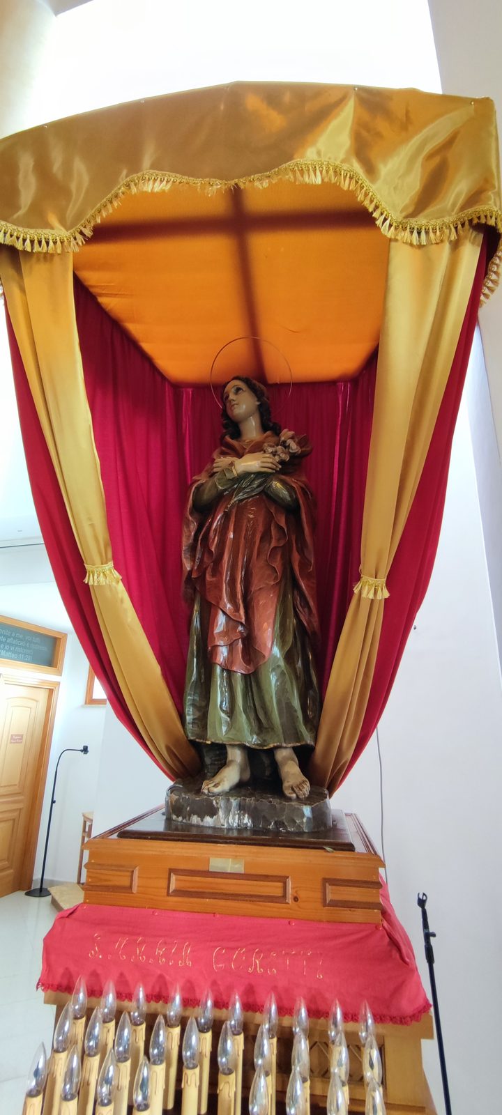Chiesa Santa Maria Goretti Statua lignea policroma di santa Maria Goretti con il giglio tra le mani, sotto un baldacchino di drappi rossi e gialli, con le candele votive alla base, nella Chiesa di Santa Maria Goretti
