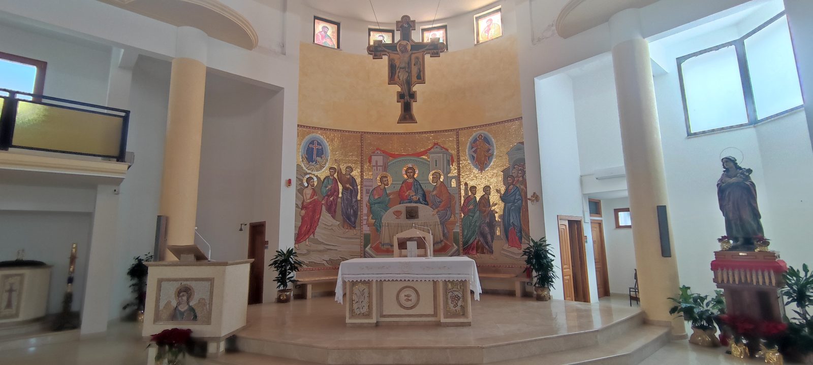 Chiesa Santa Maria Goretti Il presbiterio visto di scorcio, con l'ambone, l'altare in marmo chiaro, il crocifisso ligneo dipinto sospeso e il mosaico absidale a fondo oro, nella Chiesa di Santa Maria Goretti