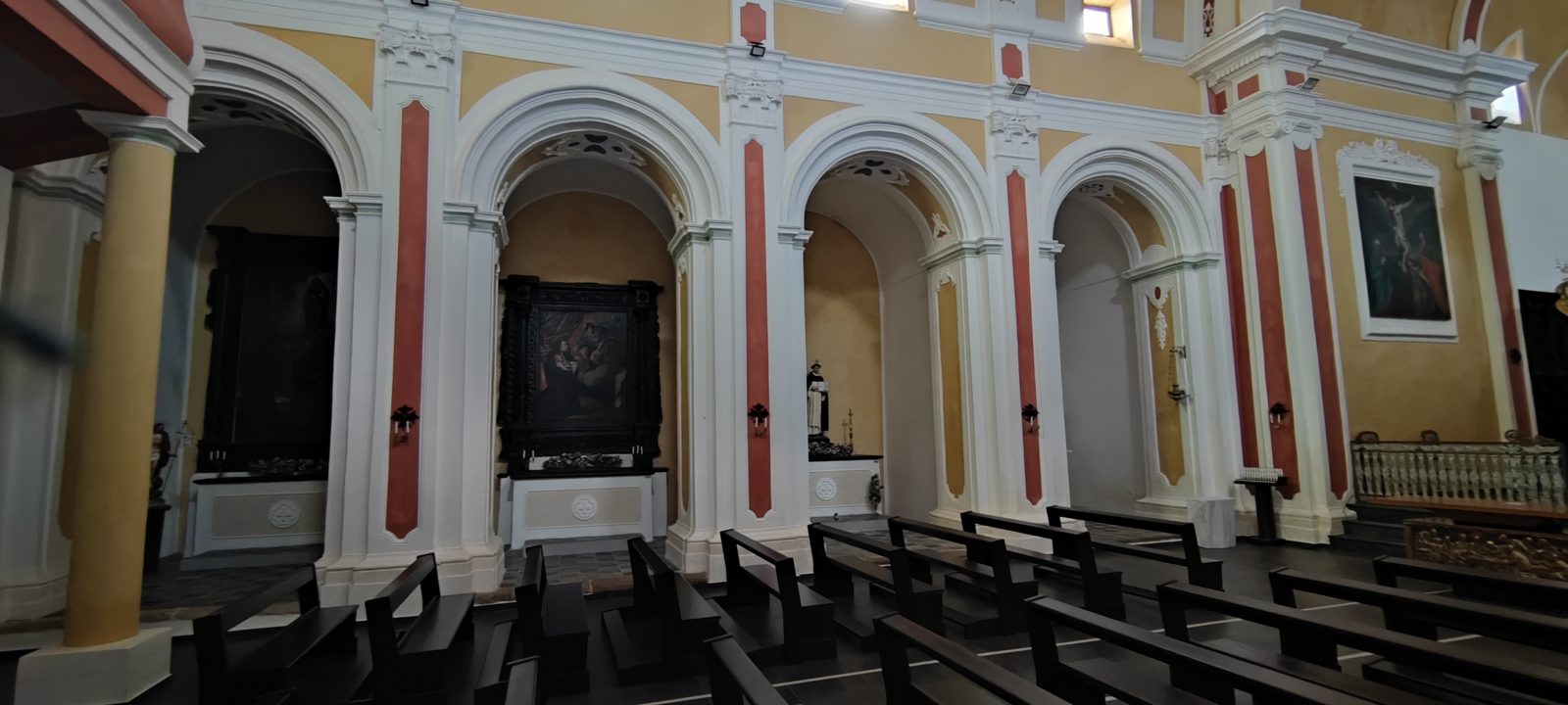 Chiesa Madonna SS. del Rosario Fila di cappelle laterali sotto archi a tutto sesto, con le tele sopra gli altari e i banchi scuri in primo piano, nella Chiesa della Madonna SS. del Rosario