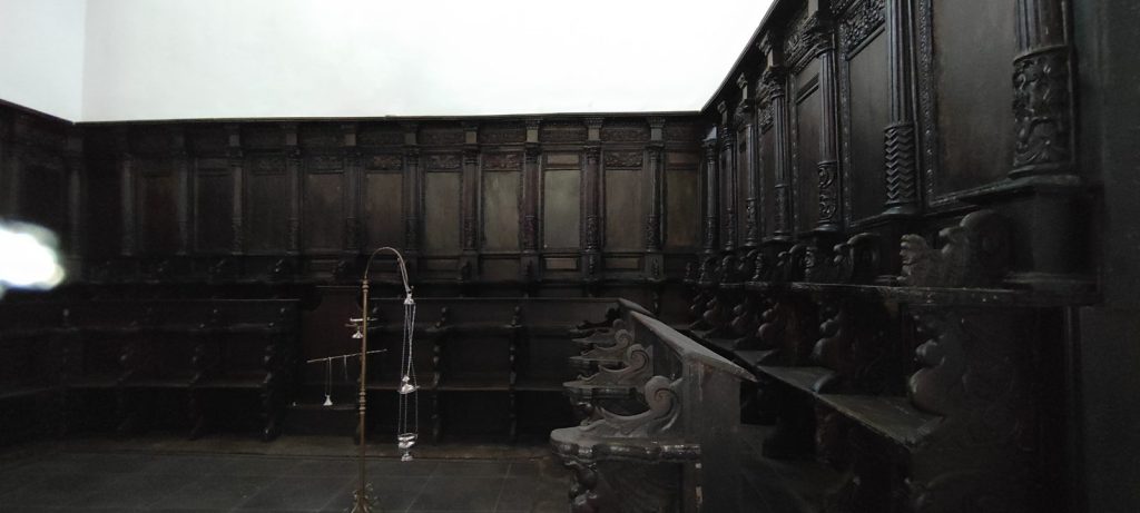 Coro ligneo seicentesco in noce scuro, con gli stalli e i braccioli intagliati lungo le pareti della sala dietro l'altare, nella Chiesa della Madonna SS. del Rosario