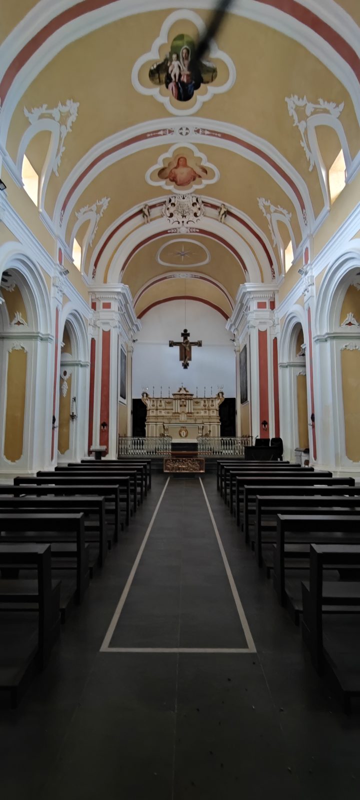 Chiesa Madonna SS. del Rosario Navata centrale con i banchi scuri rivolti all'altare maggiore e il crocifisso sull'arco, sotto la volta a botte affrescata, nella Chiesa della Madonna SS. del Rosario